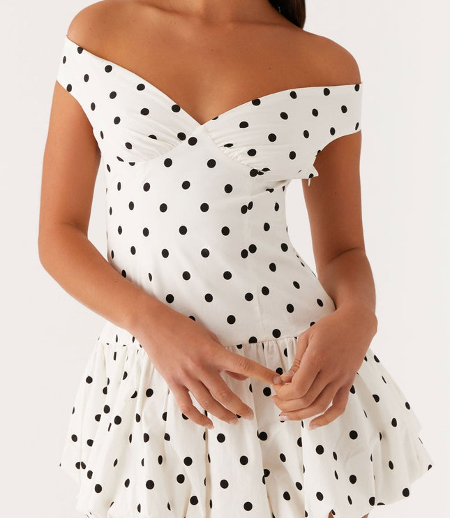Detail of a white polka dot off-shoulder mini dress, showing the ruched bust and gathered bubble hem.