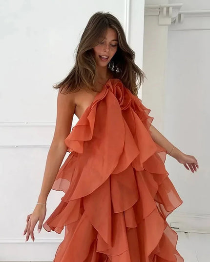 Side view of a woman in a coral strapless ruffle layered maxi dress, showing the flowing tiers and a large floral detail on the bodice.