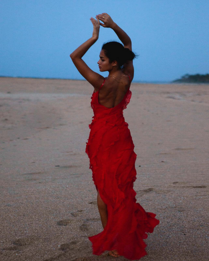 Full length view of a red V-neck ruffle side slit maxi dress with spaghetti straps on a beach at dusk
