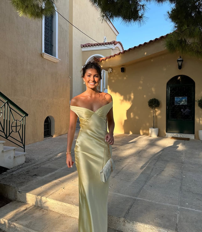 Smiling woman in a light yellow off-shoulder backless satin maxi dress, showcasing the dress's flow and elegant fit in an outdoor setting.