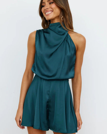 Front view of a woman wearing a sleeveless high neck satin romper in a deep teal color, featuring a draped neckline and elasticized waist.