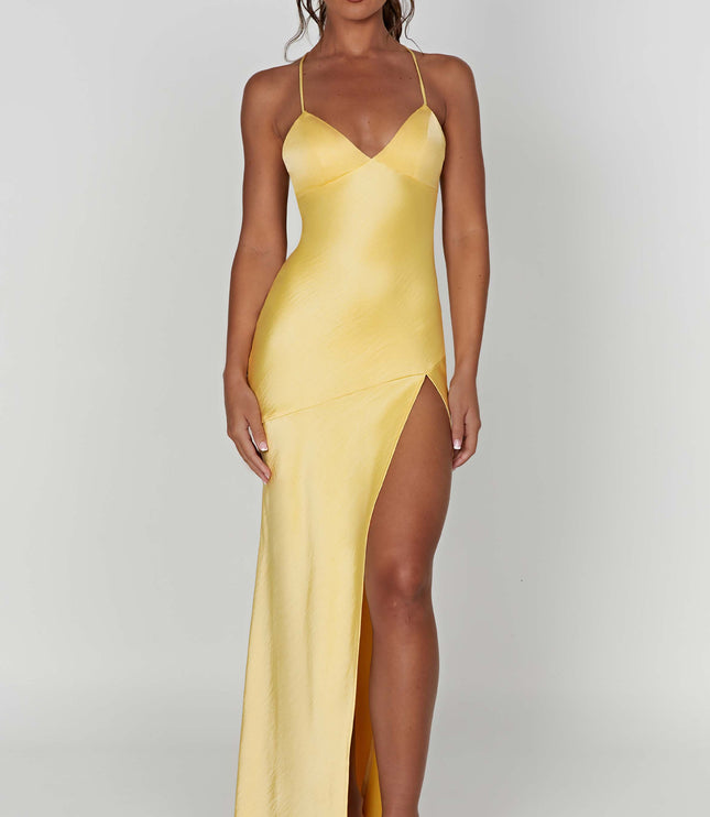 Full-length view of a women's bright yellow satin maxi dress with a V-neck, thin straps, and a high side slit, paired with nude square-toe slides.