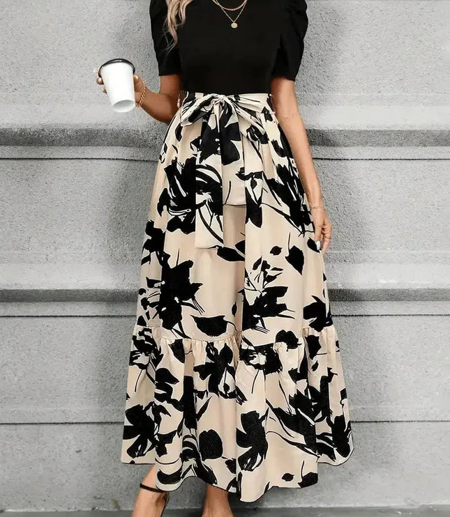 Front view of a women's high waist maxi dress with a black floral print on beige, featuring a black short sleeve top and waist tie.