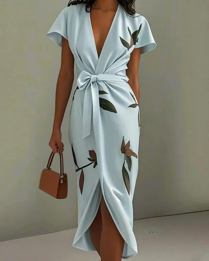 Women's light blue leaf print v-neck short sleeve midi wrap dress with a tied waist, holding a brown purse.