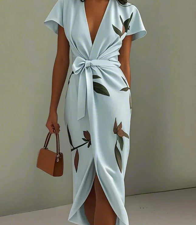 Women's light blue leaf print v-neck short sleeve midi wrap dress with a tied waist, holding a brown purse.