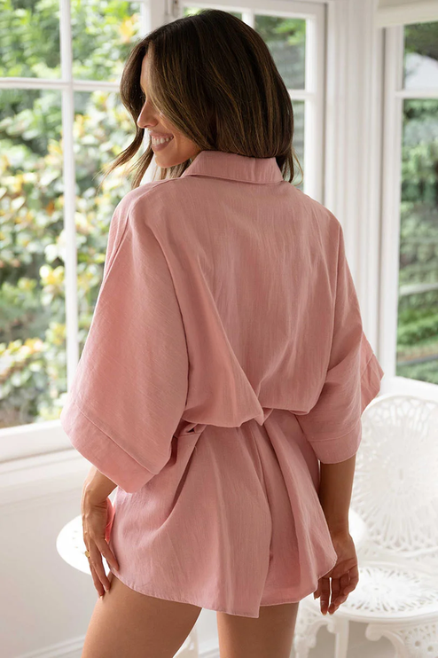 Back view of a woman wearing a pink summer collared button-front short romper, detailing the relaxed fit and tied waist.