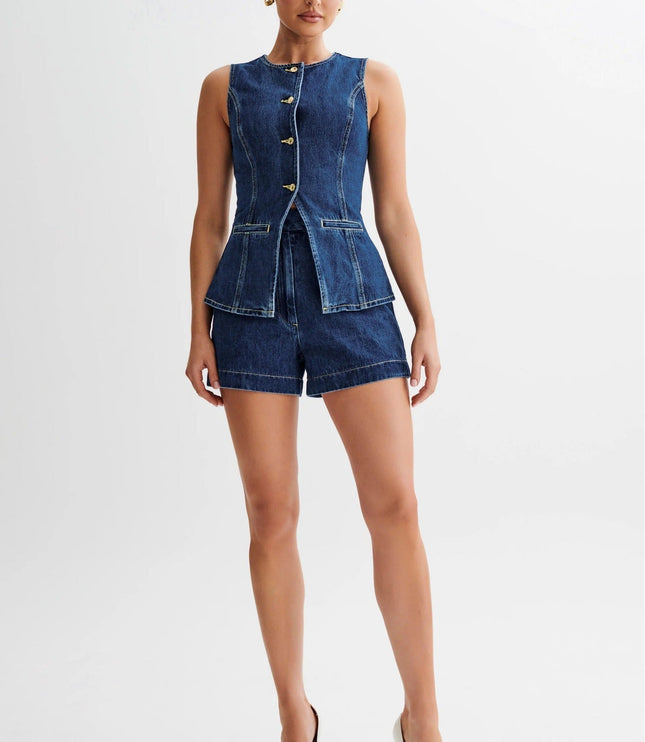 Sleeveless single breasted denim shorts set in dark wash, featuring gold buttons and a peplum waist, paired with white heels.