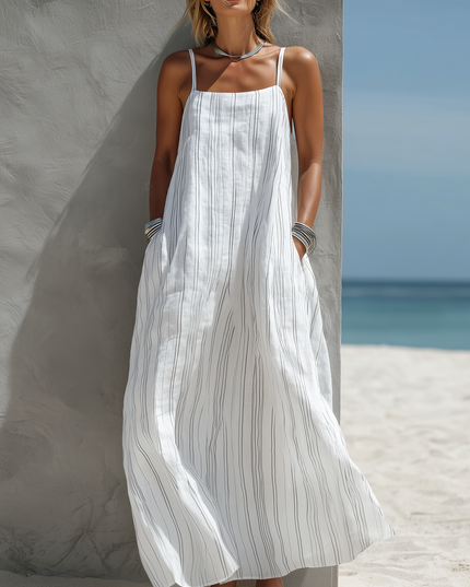 Women's white striped scoop neck sleeveless maxi dress with pockets, worn with silver bangles and necklace, on a beach.