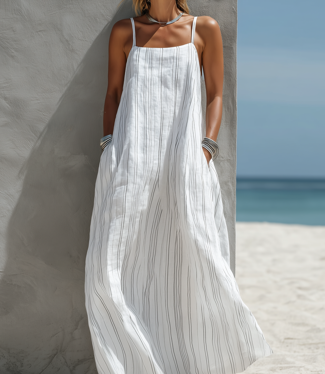 Women's white striped scoop neck sleeveless maxi dress with pockets, worn with silver bangles and necklace, on a beach.