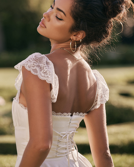 Back view of a white women's mini dress featuring delicate lace cap sleeves and a corset-style lace-up back closure.