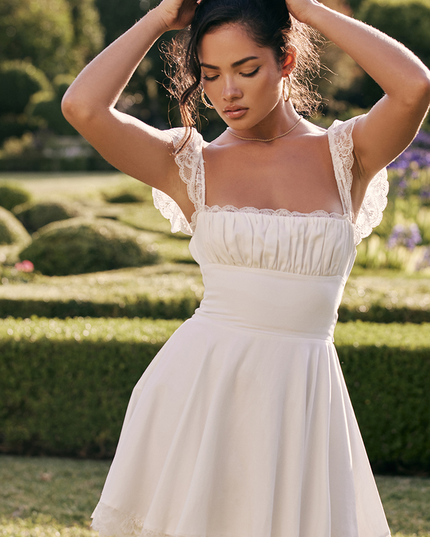 Outdoor shot of a white lace cap sleeve square neck mini dress, with the model posing in a garden setting.