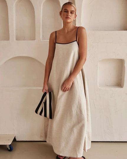 Full length view of a women's sleeveless maxi dress in light beige, with striped clutch.