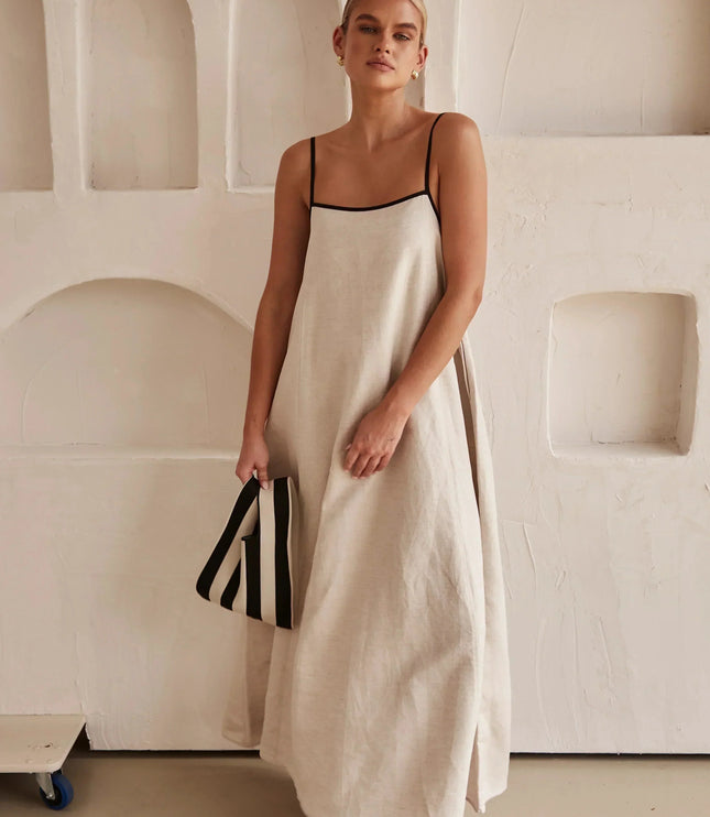 Full length view of a women's sleeveless maxi dress in light beige, with striped clutch.