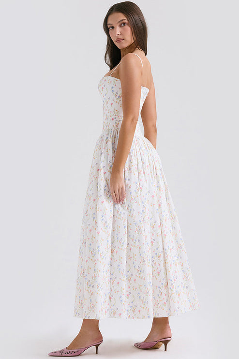 Side view of a white square neck sleeveless midi dress with delicate floral print and spaghetti straps, paired with pink heels.