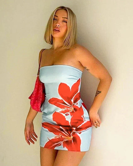 Blonde woman wearing a light blue strapless mini dress with bold red floral pattern, holding a pink bag.