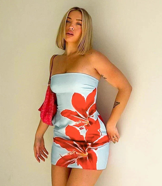 Blonde woman wearing a light blue strapless mini dress with bold red floral pattern, holding a pink bag.