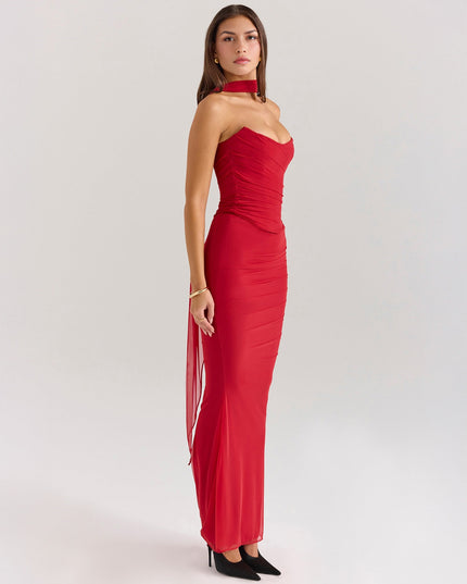 Side profile of red strapless ruched maxi dress with long flowing sheer panel, black heels.