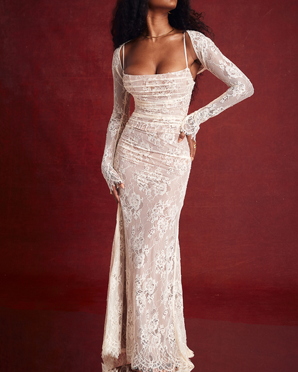 White lace strapless maxi dress with long sleeve bolero, ruched bodice, and floral lace overlay, against a red backdrop.