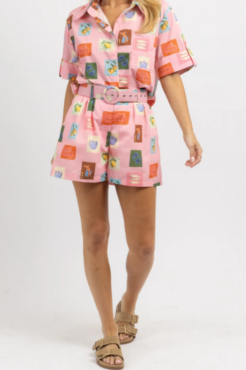 Front view of women's pink summer short set with a playful fruit and vase print, paired with gold slides.