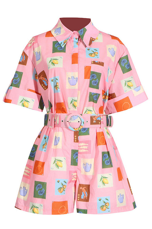 Flat lay of pink short sleeve shirt and shorts set with a unique fruit and vase pattern and a matching belt.
