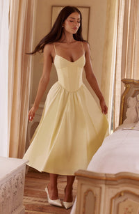 Light yellow sweetheart corset midi dress with spaghetti straps and full skirt, worn with white heels.