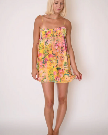Full body shot of a woman wearing a yellow floral print tie shoulder mini dress with delicate spaghetti straps.