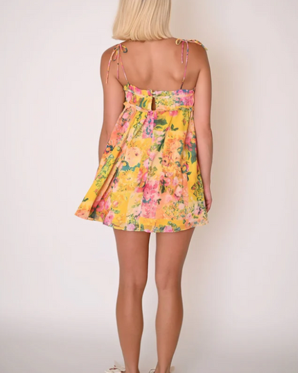 Back view of a woman wearing the yellow floral print tie shoulder mini dress, highlighting the flowy skirt.