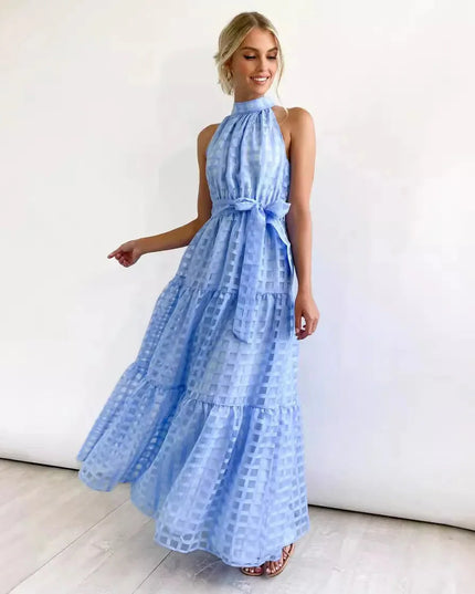 Smiling woman in a light blue halter neck tiered maxi dress, featuring a delicate checkered pattern and waist tie.