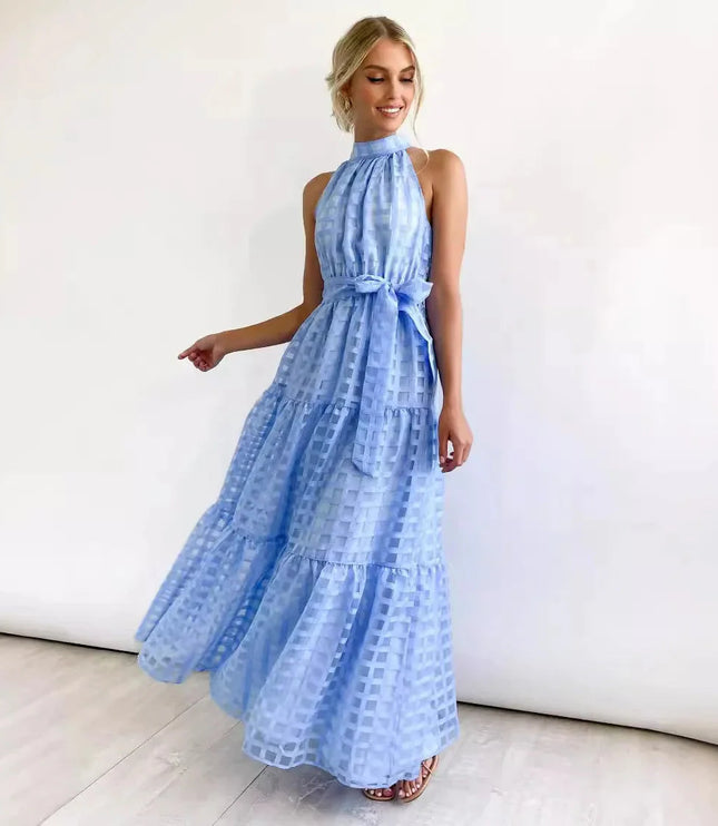 Smiling woman in a light blue halter neck tiered maxi dress, featuring a delicate checkered pattern and waist tie.