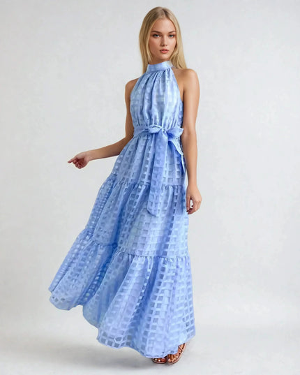 Blonde woman wearing a light blue halter neck tiered maxi dress with a delicate checkered pattern and waist tie.