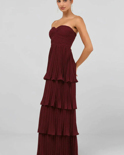 Side profile of the women's strapless tiered pleated maxi dress in burgundy, highlighting the flowing pleats.