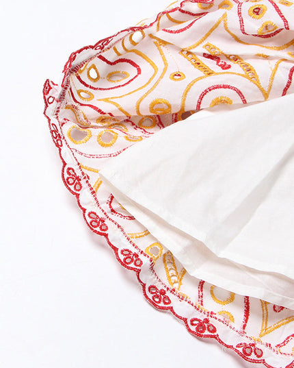 Inside view of the tiered hem of a women's mini dress, the white lining and red and yellow embroidery.