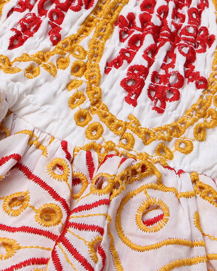 Close up of the transition from shirred bodice to tiered skirt on a women's embroidered mini dress, showcasing the red and yellow designs.