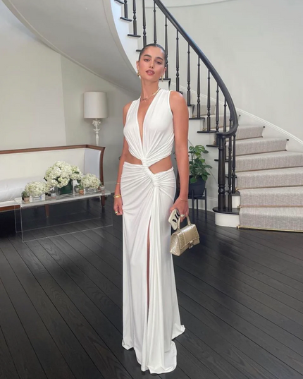 White sleeveless halter V-neck maxi dress with side cut-outs and a high slit, standing indoors.