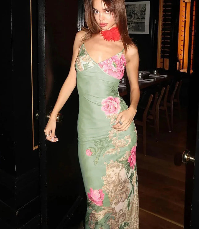 Full-length women's floral print V-neck maxi dress in sage green with large pink flowers and ornate scrollwork, shown in a doorway.
