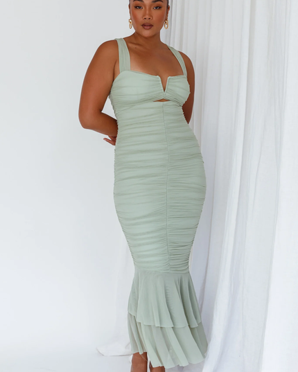 Front full-length view of a woman wearing a light green ruched V-neck fishtail maxi dress with clear heels.